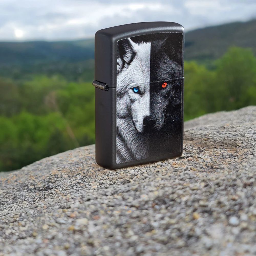 Lifestyle image of Zippo Two Wolves Design Black Matte Windproof Lighter standing on a rock with hills in the background.