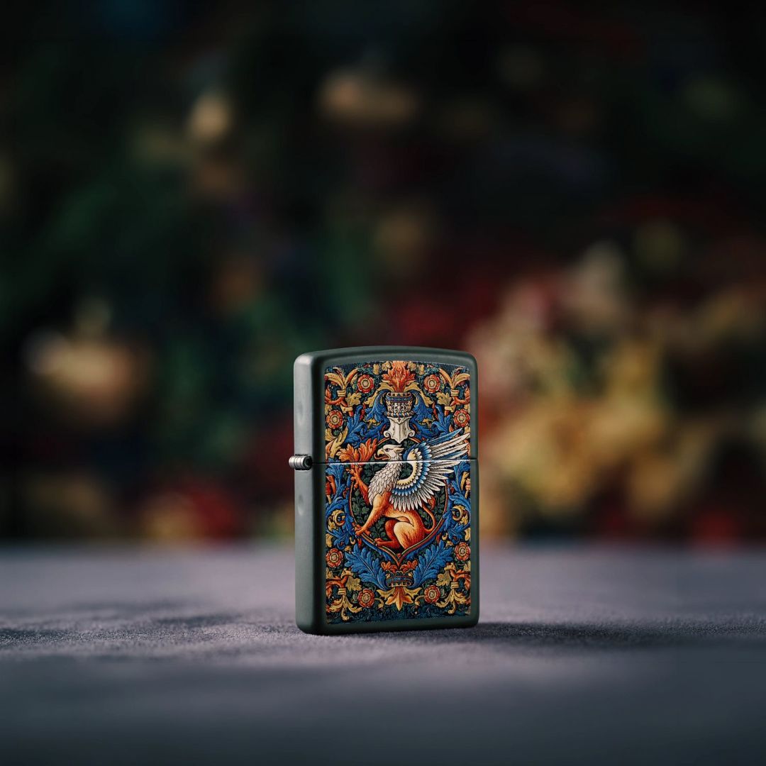 Lifestyle image of Zippo Gryphon Design Green Matte Windproof Lighter standing on a black fabric surface showing the front and hinge side of the lighter with an out of focus dark muted floral background. 


