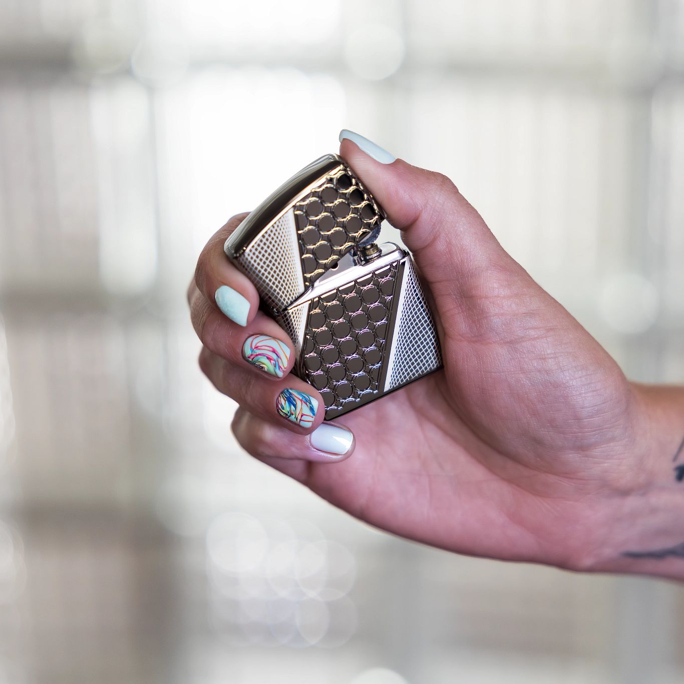 Lifestyle image of Zippo Deep Dots Design Armor® Black Ice® Windproof Lighter being held in a hand, slightly opened, with a blurred glass wall background. 

