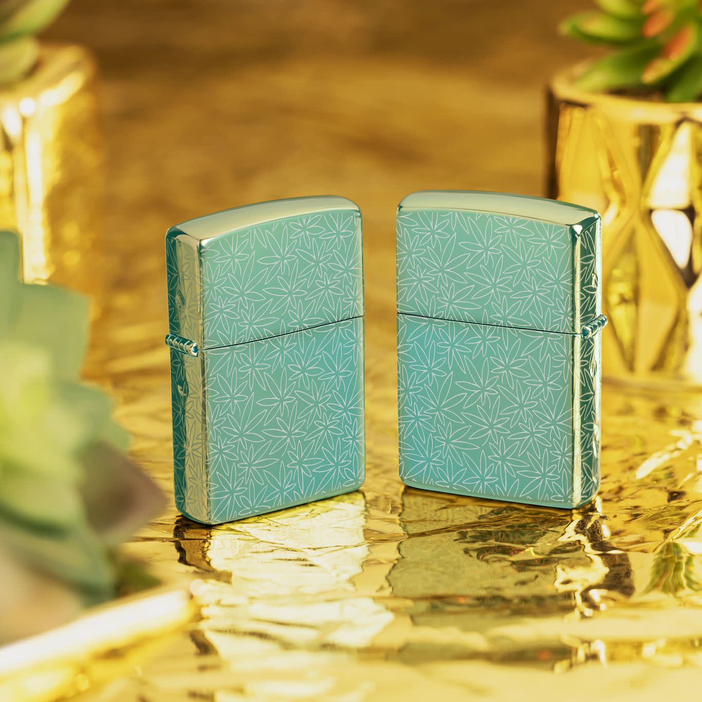 Lifestyle image of two Zippo Atomic Cannabis Design High Polish Green Windproof Lighters standing on a golden surface with succulents in golden pots behind them.