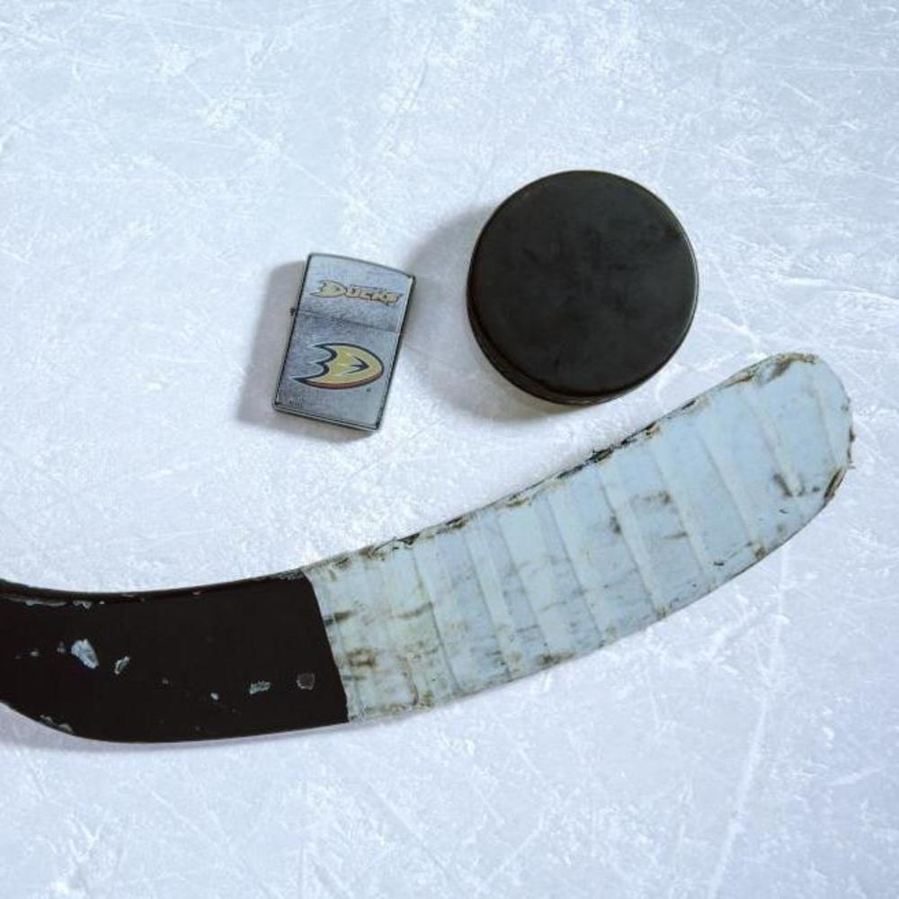 Lifestyle image of the NHL Anaheim Ducksr Street Chrome Windproof Lighter laying on ice with a hockey puck and stick