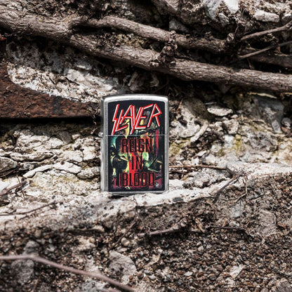 Lifestyle image of Zippo Slayer Reign in Blood Design Street Chrome Windproof Lighter standing on a rocky surface showing the front of the lighter with rocks and twigs in the background. 

