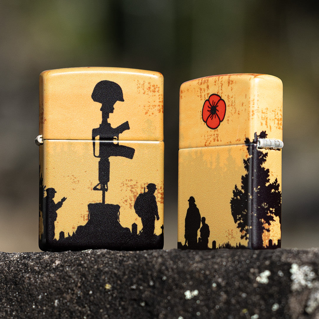 Lifestyle image of two Zippo 2025 Veterans Day Commemorative 540 Matte Windproof Lighters standing on a black rock, one lighter is showing the front of the design while the other shows the back and hinge side of the lighter. 

