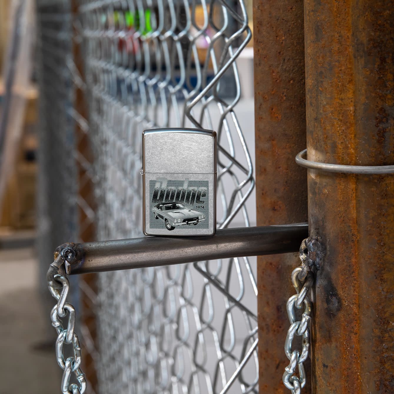 Lifestyle image of Zippo Dodge Challenger Design Street Chrome Windproof Lighter standing next to a chain link fence.