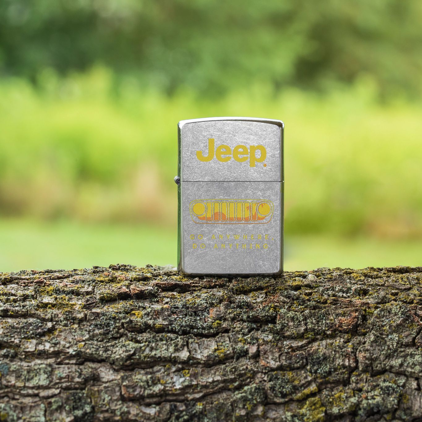 Lifestyle image of Zippo Jeep® Grille Design Street Chrome Windproof Lighter standing on a tree trunk with an overgrown field in the background.

