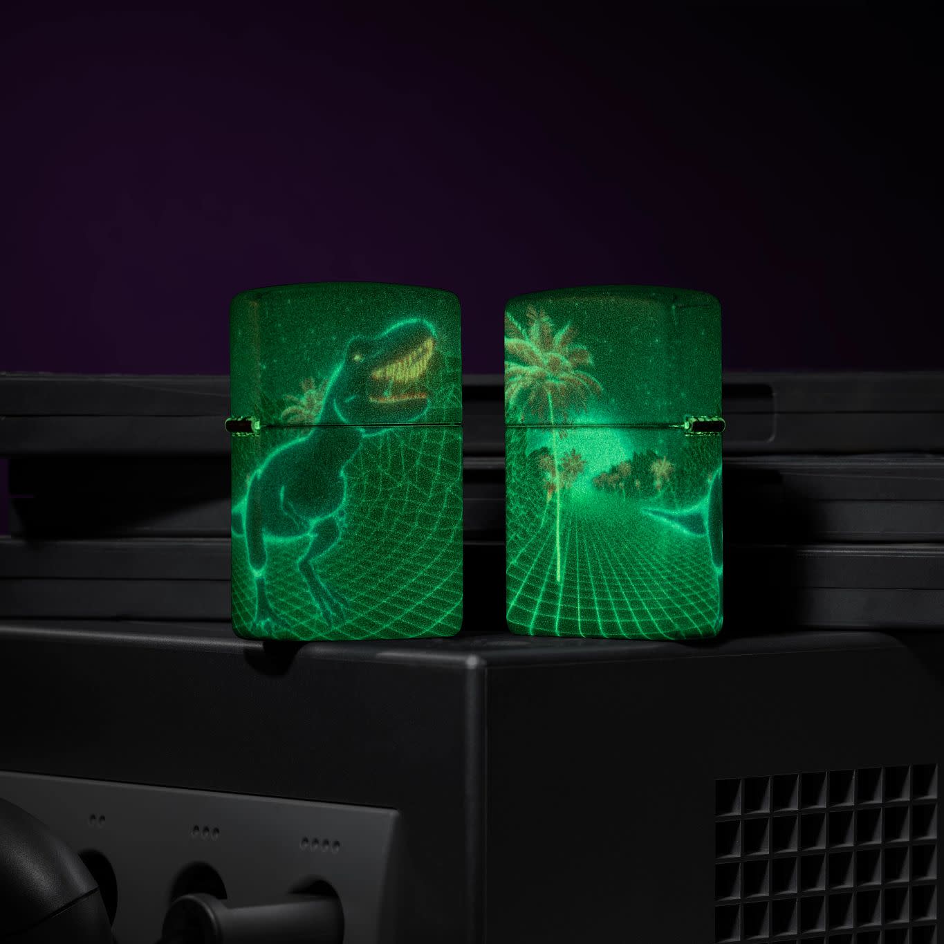 Lifestyle image of two Zippo Cyber Dino Design Glow in the Dark Windproof Lighters standing on a retro gaming system glowing in the dark.