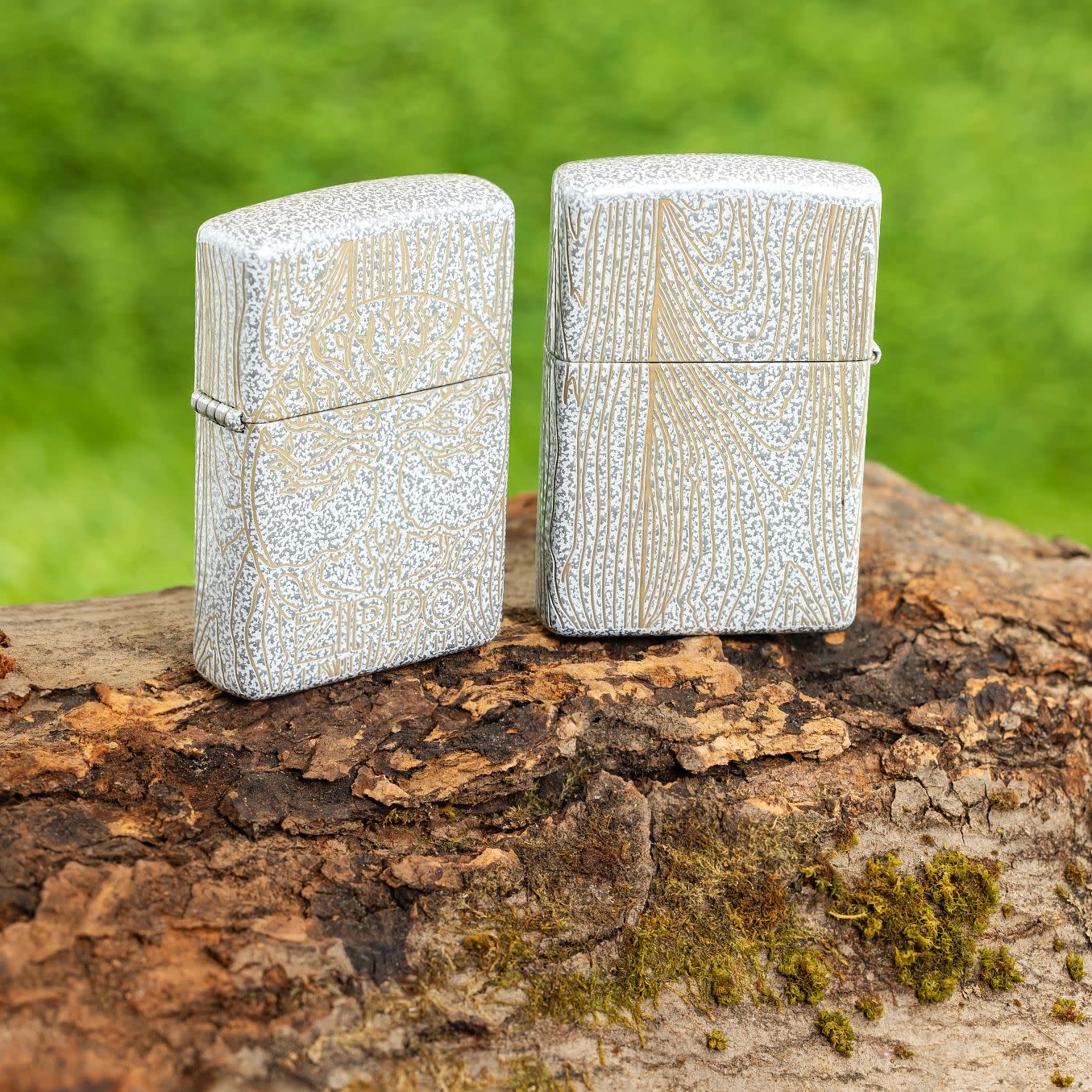 Lifestyle image of two Zippo Tree of Life Woodgrain Design Glacier Windproof Lighters standing on a log with grass in the background.