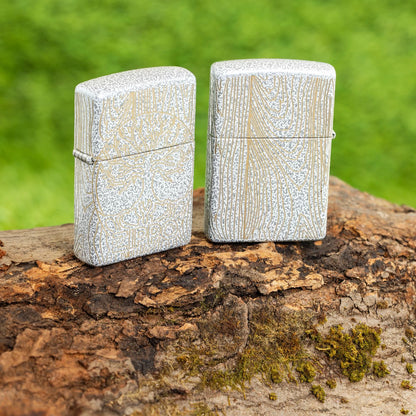 Lifestyle image of two Zippo Tree of Life Woodgrain Design Glacier Windproof Lighters standing on a log with grass in the background.