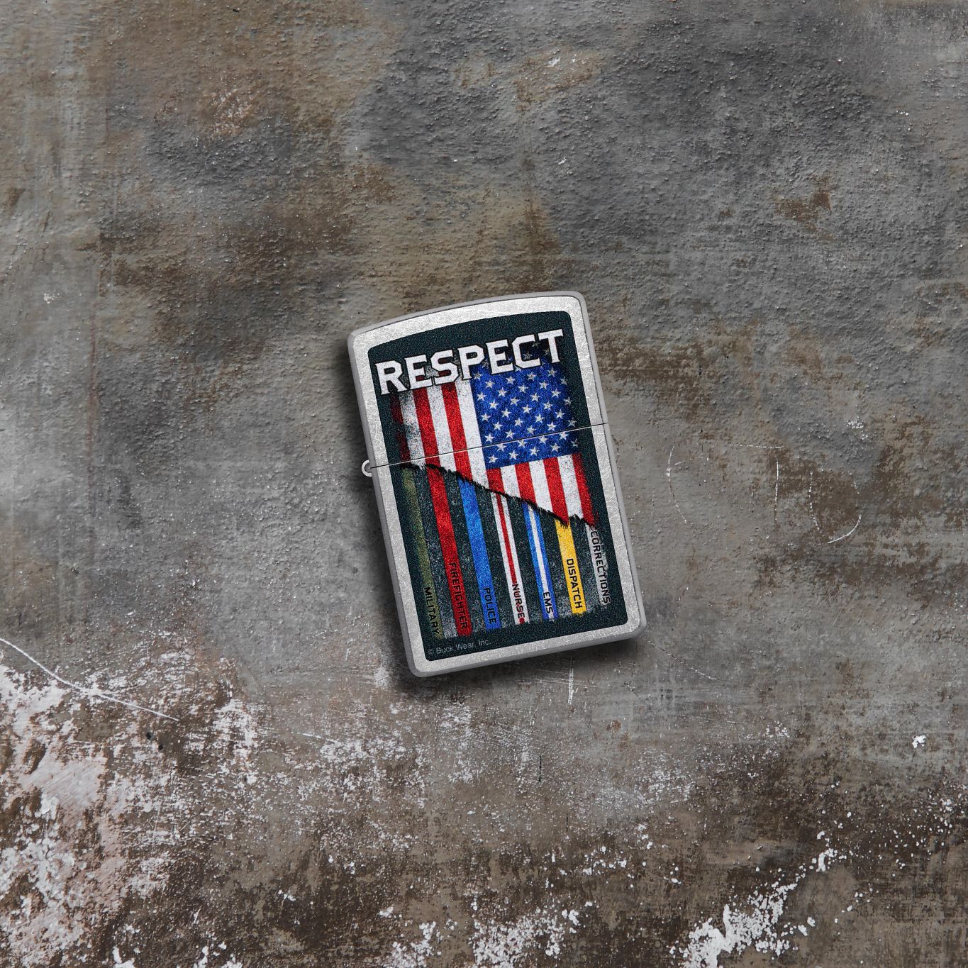 Lifestyle image of Zippo Buck Wear™ Respect Design Street Chrome Windproof Lighter lying on concrete while showing the front of the lighter. 

