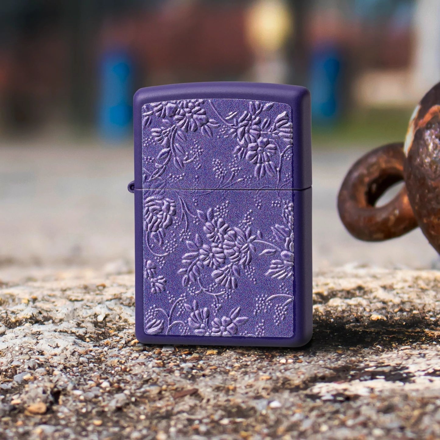 Lifestyle image of Zippo Texture Bouquet Design Purple Matte Windproof Lighter standing on a rocky surface next to a rusty shackle, while showing the front of the lighter. 


