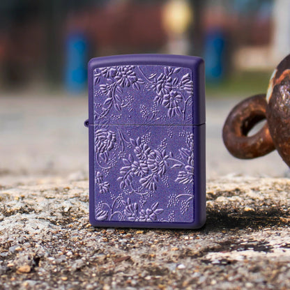 Lifestyle image of Zippo Texture Bouquet Design Purple Matte Windproof Lighter standing on a rocky surface next to a rusty shackle, while showing the front of the lighter. 

