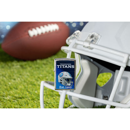 Lifestyle image of Zippo NFL Tennessee Titans Helmet Design Street Chrome Windproof Lighter standing on the facemask of a white helmet showing the front of the lighter with a football lying on a football field as the background.