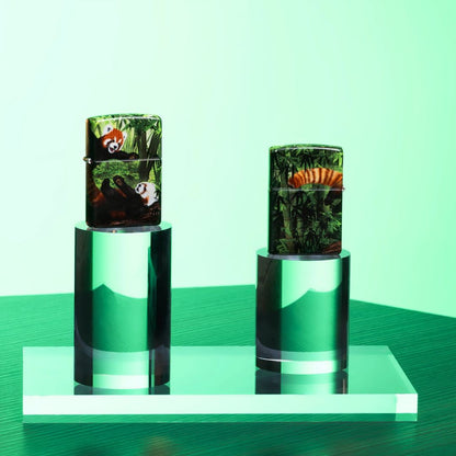 Lifestyle image of two Zippo Panda Party Design 540 matte Windproof Lighters both standing on a clear stand, one showing the front of the lighter while the other is showing the back of the lighter with a light green background. 

