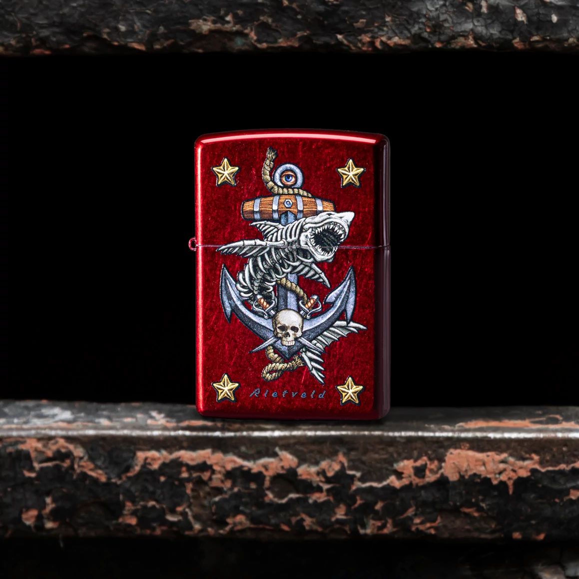 Lifestyle image of Zippo Rietveld Anchor Design Candy Apple Red Windproof Lighter standing in the gap of a gate showing the front of the lighter. 

