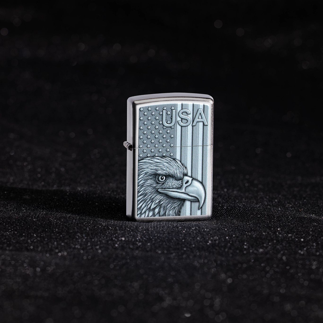 Lifestyle image of Zippo USA Pride Design Satin Chrome Windproof Lighter standing showing the front of the lighter with a black shimmer fabric background. 