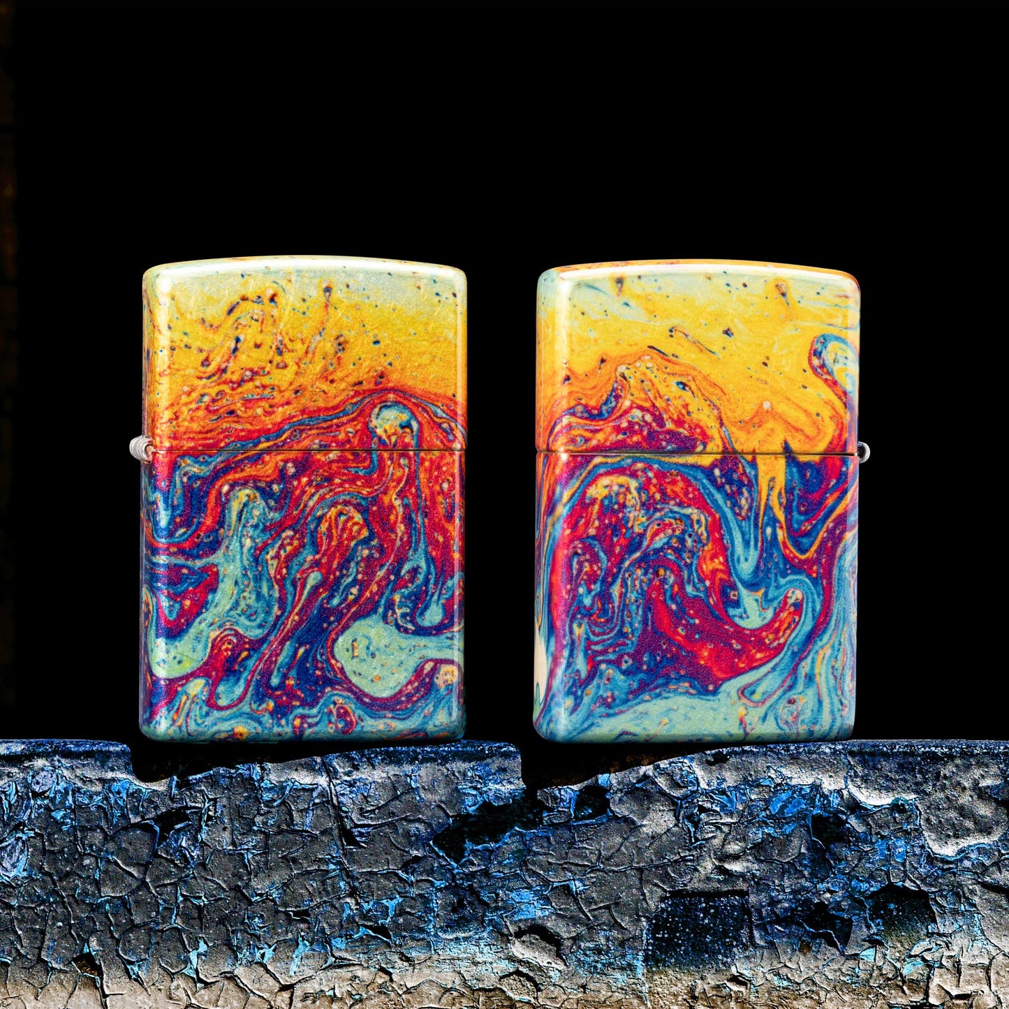 Lifestyle image of two Zippo Magma Fusion Design 540 Tumbled Brass Windproof Lighters, one showing the front of the lighter while the other shows the back of the lighter while standing on a weathered painted surface and a black background. 

