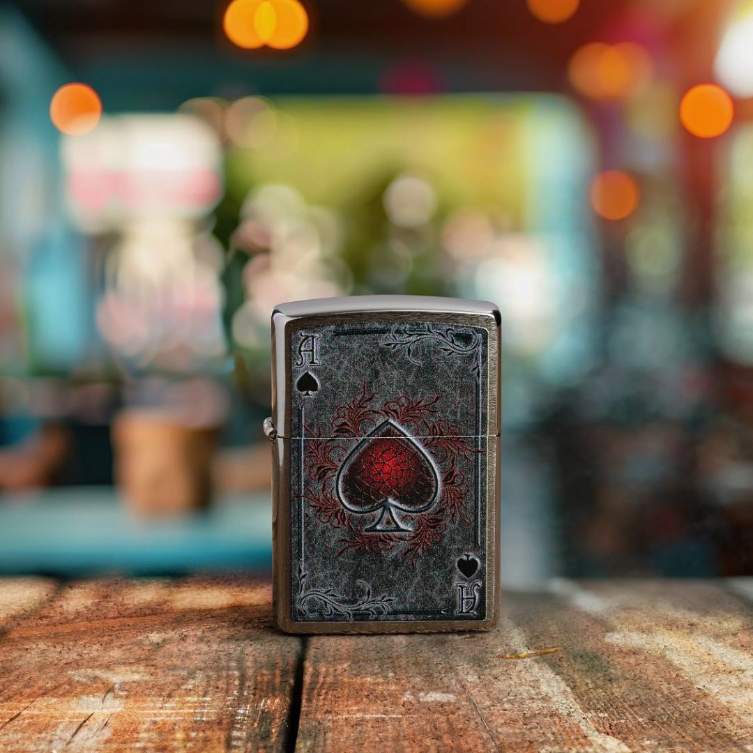 Lifestyle image of Zippo Antiqued Ace Design Brushed Chrome Windproof Lighter standing on an old wooden table showing the front of the lighter with an out of focus bar or restaurant as the background. 

