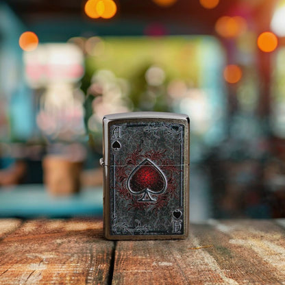 Lifestyle image of Zippo Antiqued Ace Design Brushed Chrome Windproof Lighter standing on an old wooden table showing the front of the lighter with an out of focus bar or restaurant as the background. 

