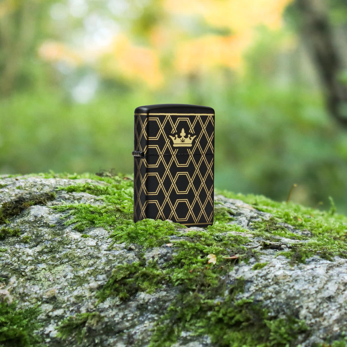 Lifestyle image of Zippo Queen Of Bud Geometric Design Black Matte Windproof Lighter standing on a mossy rock with blurred vegetation in the background.