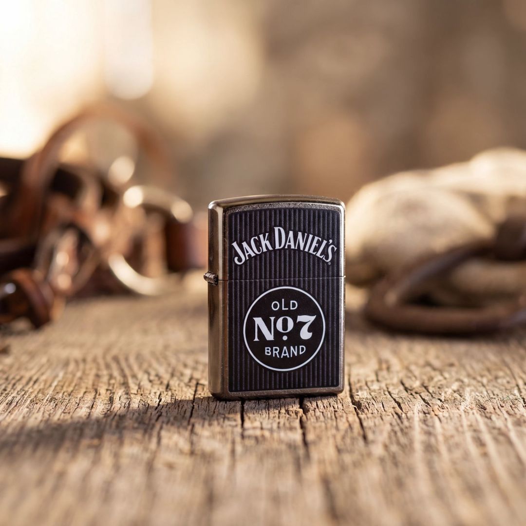 Lifestyle image of Zippo Jack Daniel's Old No. 7 Pinstripe Design Street Chrome Windproof Lighter standing on a wooden table showing the front of the lighter with an out of focus background. 

