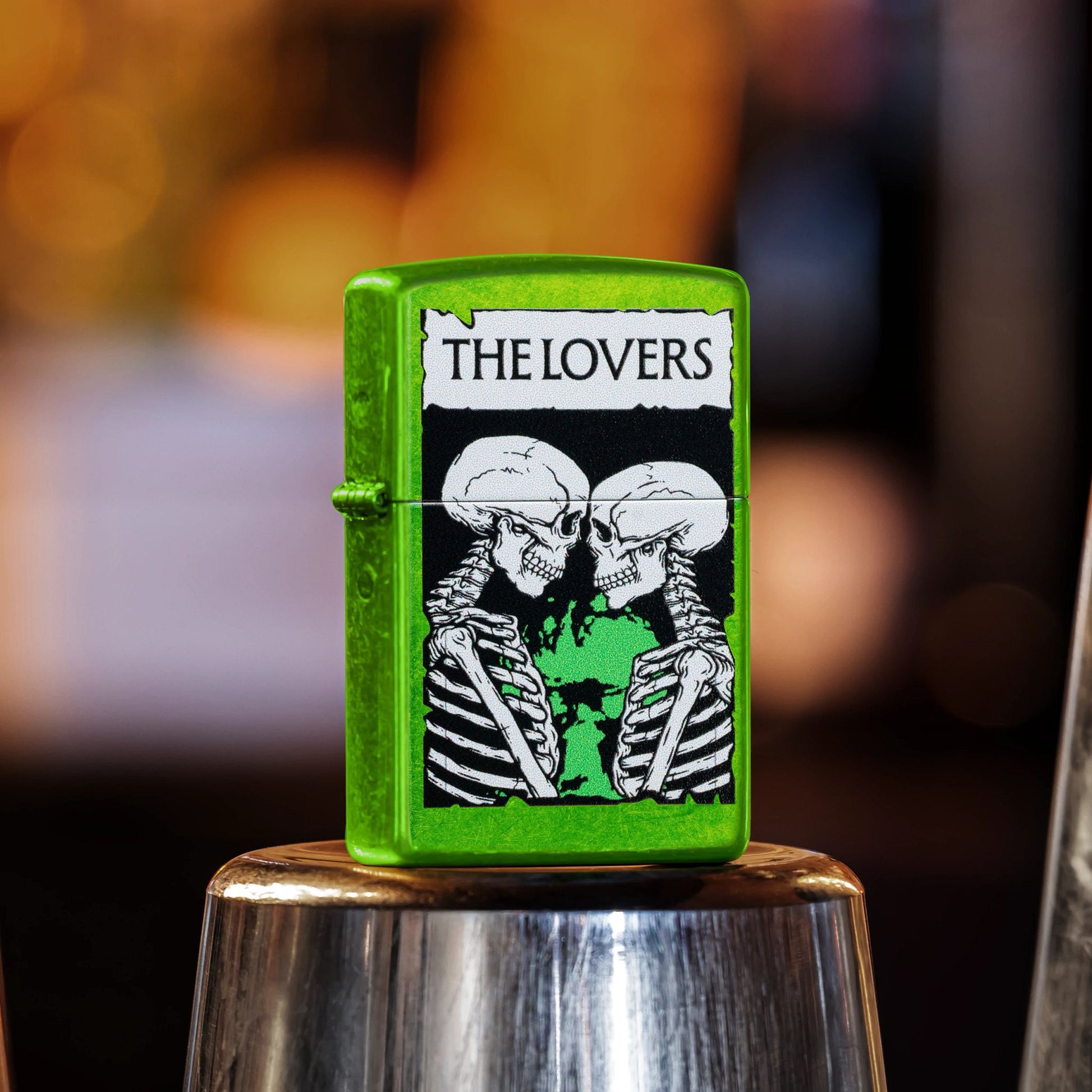 Lifestyle image of Zippo The Lovers Design Lurid Windproof Lighter standing on the bottom of a cocktail shaker showing the front and hinge side of the lighter. 