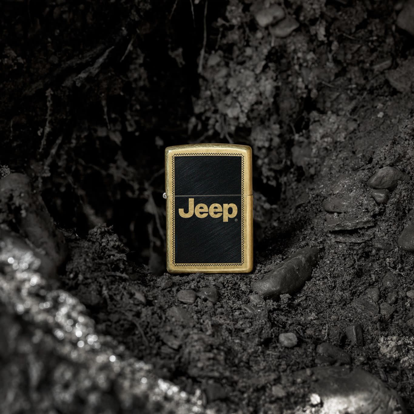 Lifestyle image of Zippo Jeep Stamp Design Regular Street Brass Windproof Lighter standing in a rocky hole in the ground.