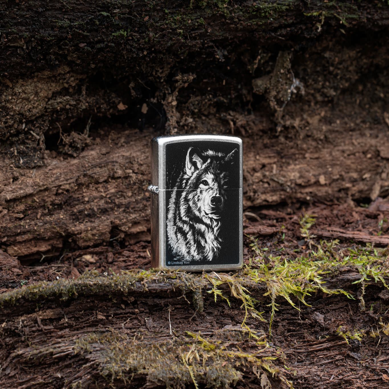 Lifestyle image of Zippo Lindsay Kivi Shadow Wolf Street Chrome Windproof Lighter standing on a mossy outdoor background.