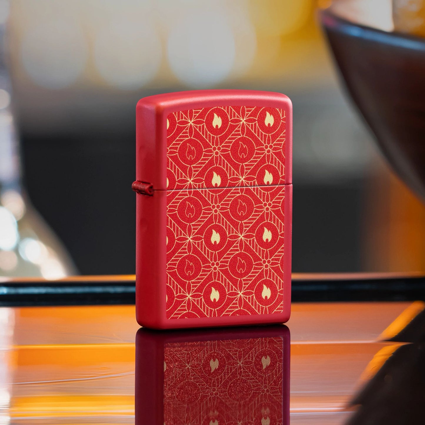 Lifestyle image of Zippo Festive Flame Design Red Matte Windproof Lighter standing on a bar showing the front and hinge side of the lighter. 

