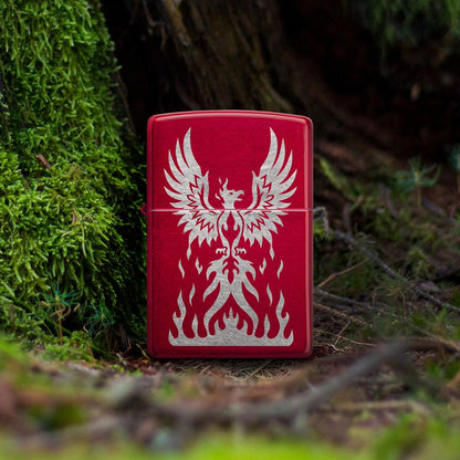 Lifestyle image of Zippo Phoenix Rising Design Candy Apple Red Windproof Lighter standing at the base of a moss-covered tree stump, showing the front of the lighter. 

