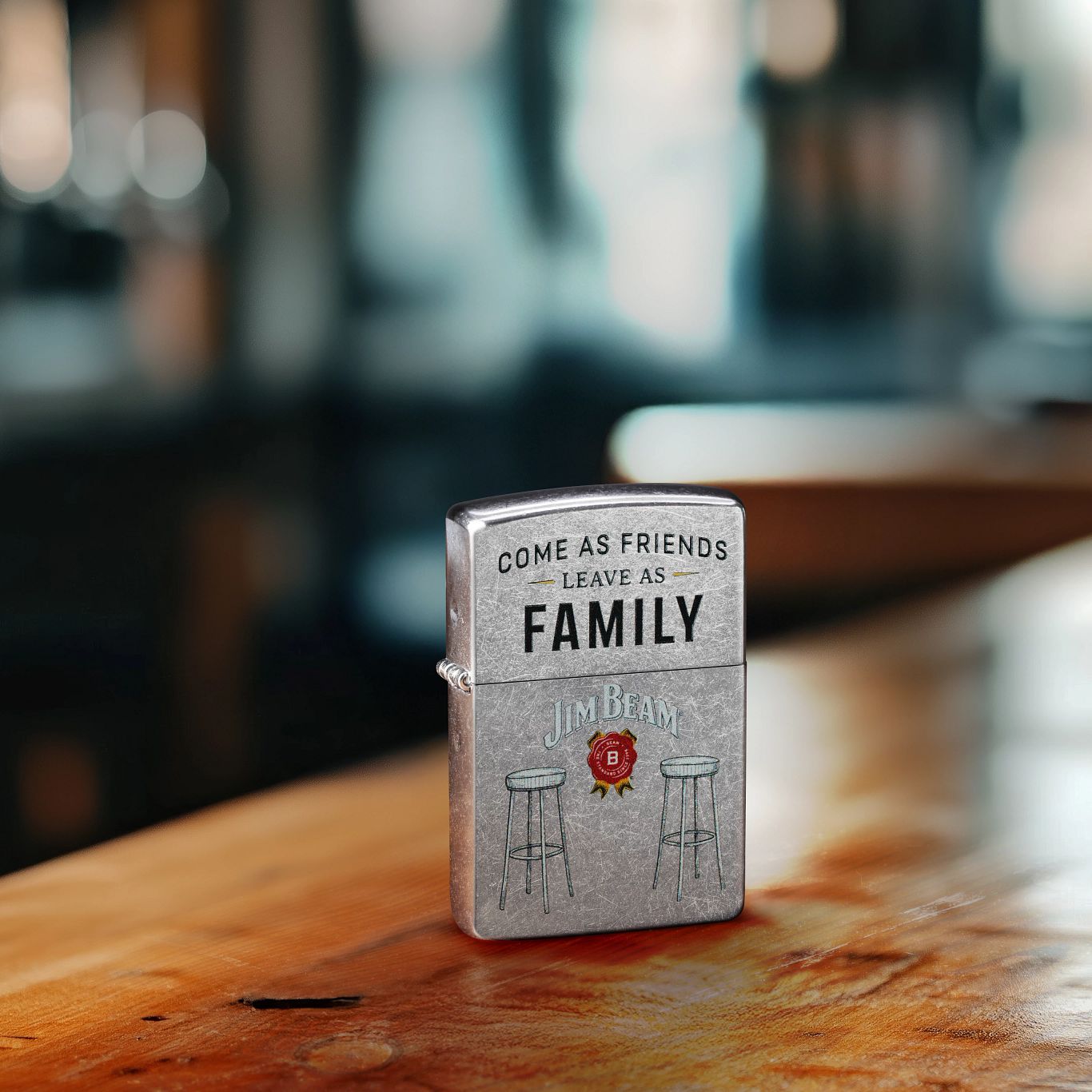 Lifestyle image of Zippo Jim Beam® Barstools Design Street Chrome Windproof Lighter standing on a bar with the pub blurred in the background. 