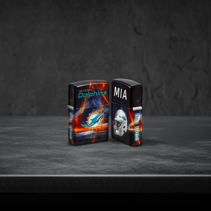 Lifestyle image of two Zippo NFL Miami Dolphins 540 Matte Windproof Lighters, one showing the front of the lighter and the other showing the back, standing on a dark grey surface.