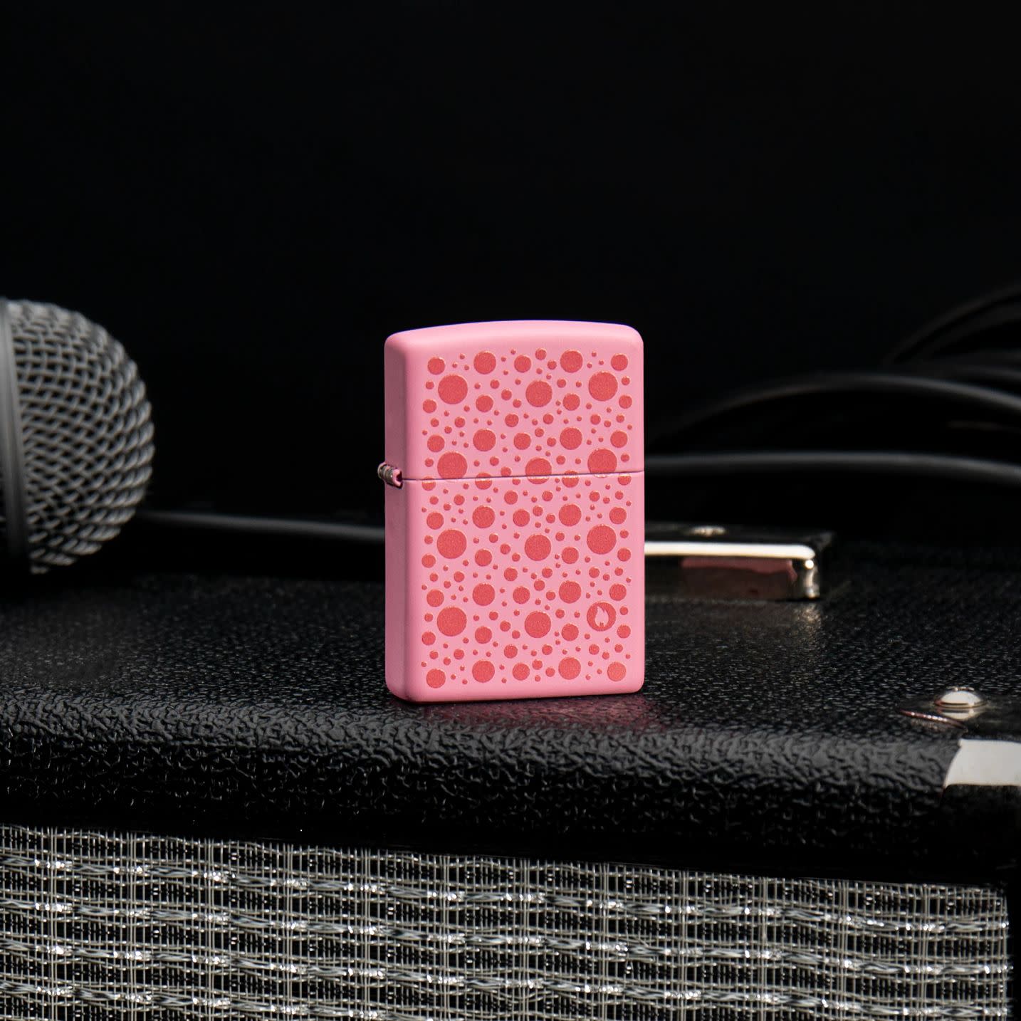 Lifestyle image of Zippo Polka Dot Design Pink Matte Windproof Lighter standing with a speaker and microphone.