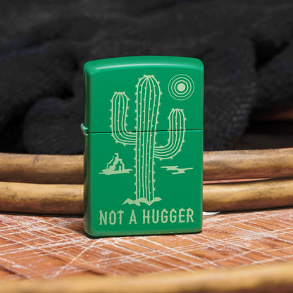 Lifestyle image of Zippo Not a Hugger Design Grass Green Matte Windproof Lighter standing on a wooden surface in front of a few power cords, showing the front of the lighter. 

