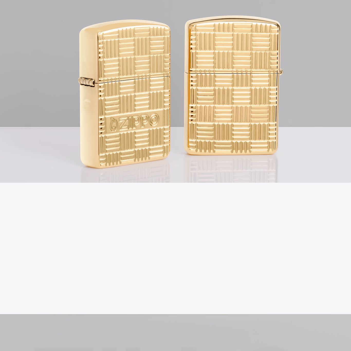 Lifestyle image of two Zippo Deep Carve Design Armor High Polish Brass Windproof Lighters standing on a white shelf: one showing the front of the lighter, one showing the back.