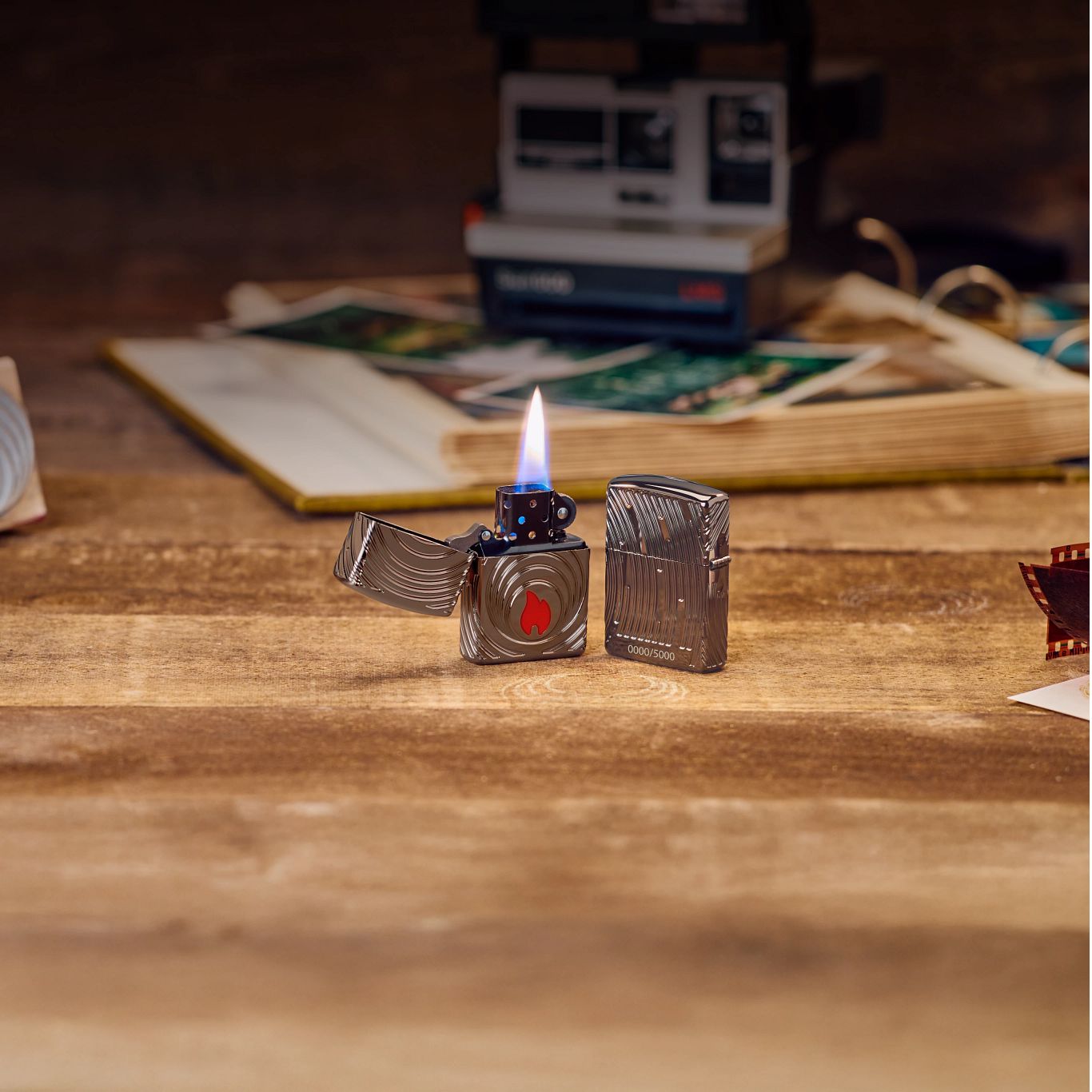 Lifestyle image of two Zippo 2026 Collectible of the Year Windproof Lighters; one open and lit showing the front of the lighter and the other showing the back and hinge side of the lighter, both standing on a table with an old photo album and polaroid camera.


