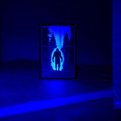 Lifestyle image of Zippo Ultra Squatch Design Black Matte Windproof Lighter standing on a dark surface under a black light. 

