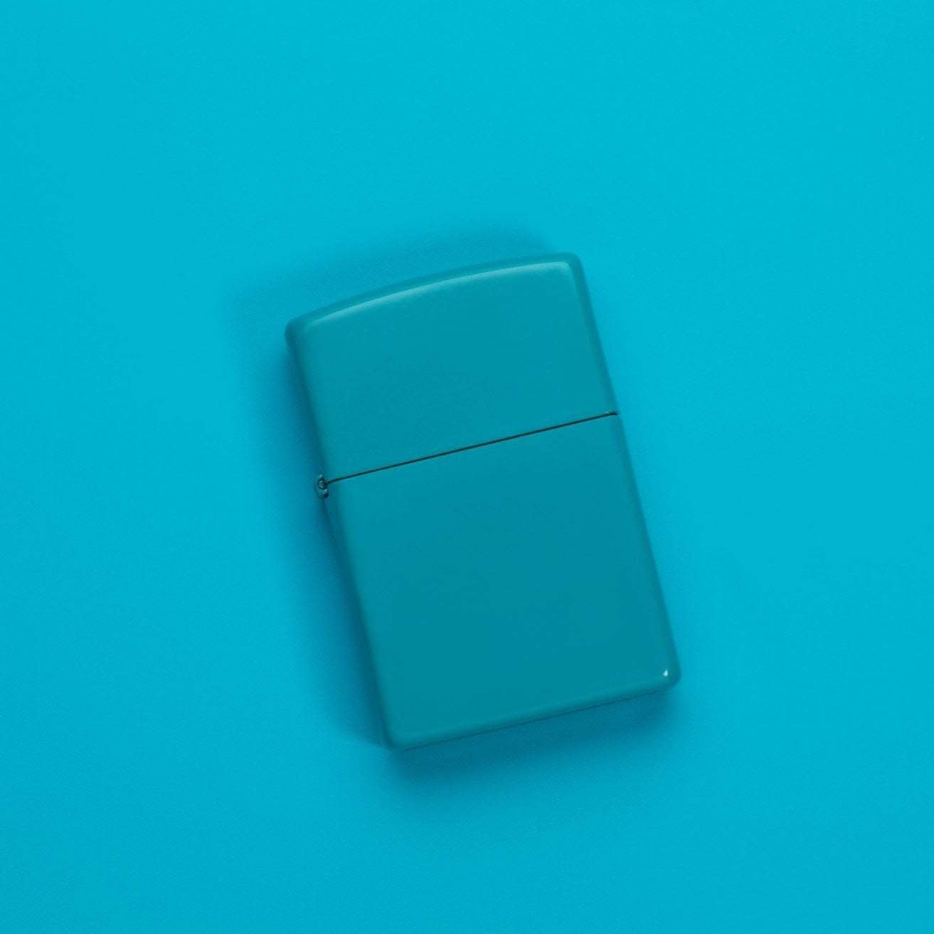 Lifestyle image of Classic Flat Turquoise Windproof Lighter laying on a turquoise surface