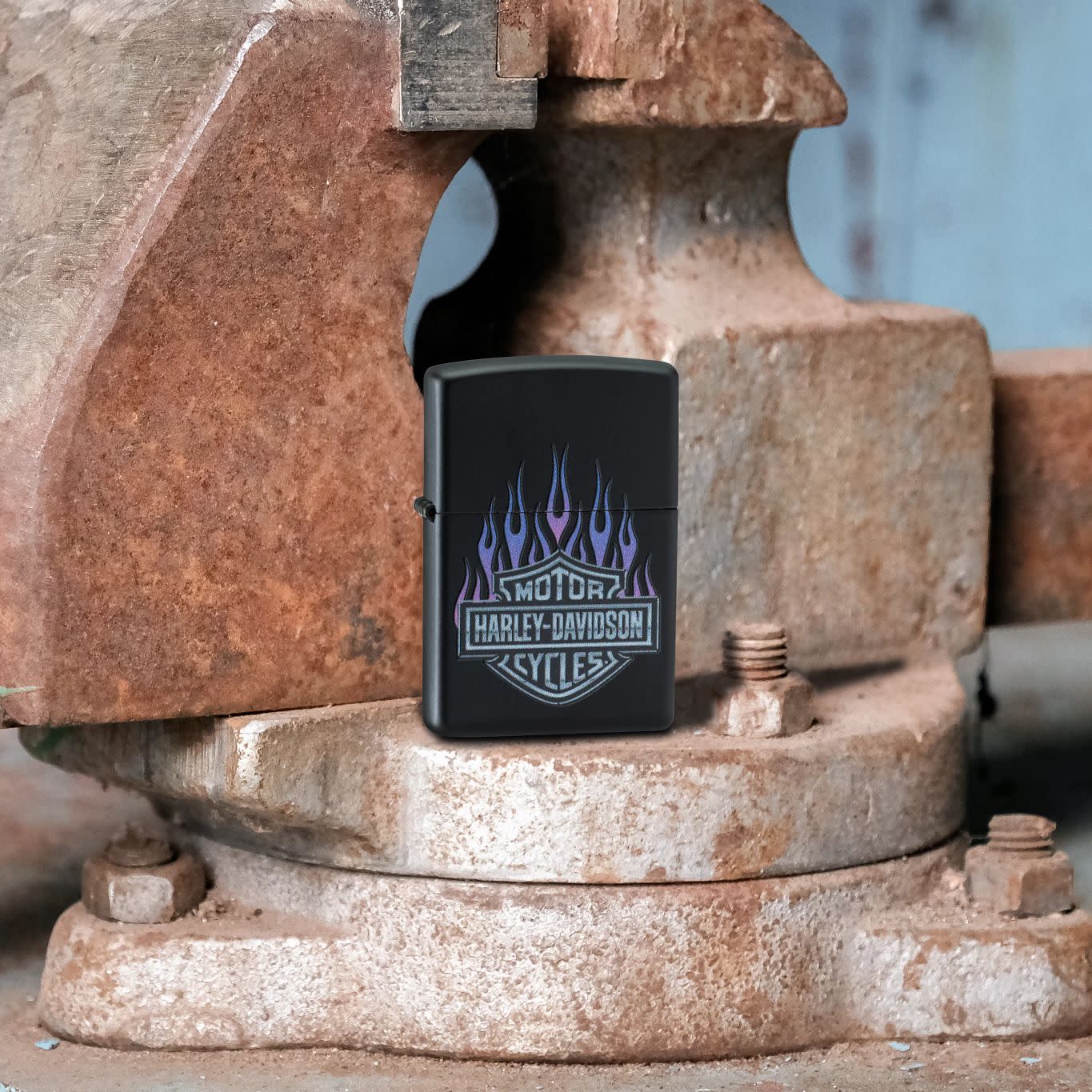 Lifestyle image of Zippo Harley Davidson® Flames Black Matte Windproof Lighter standing on a rusty vise.