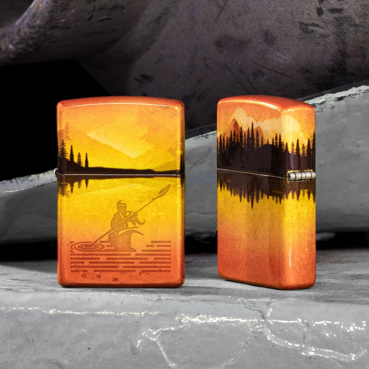 Lifestyle image of two Zippo Fishing Fusion Design 540 Tumbled Brass Windproof Lighters; One showing the front of the lighter and the other showing the back and hinge side of the lighter, both standing on a metal surface with pieces of metal in the background. 

