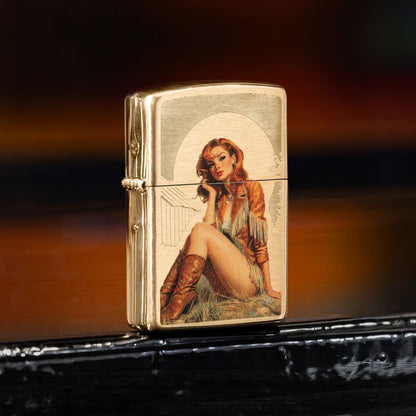 Lifestyle image of Zippo Western Pinup Design Brushed Brass Windproof Lighter standing on a black windowsill showing the front and hinge side of the lighter. 

