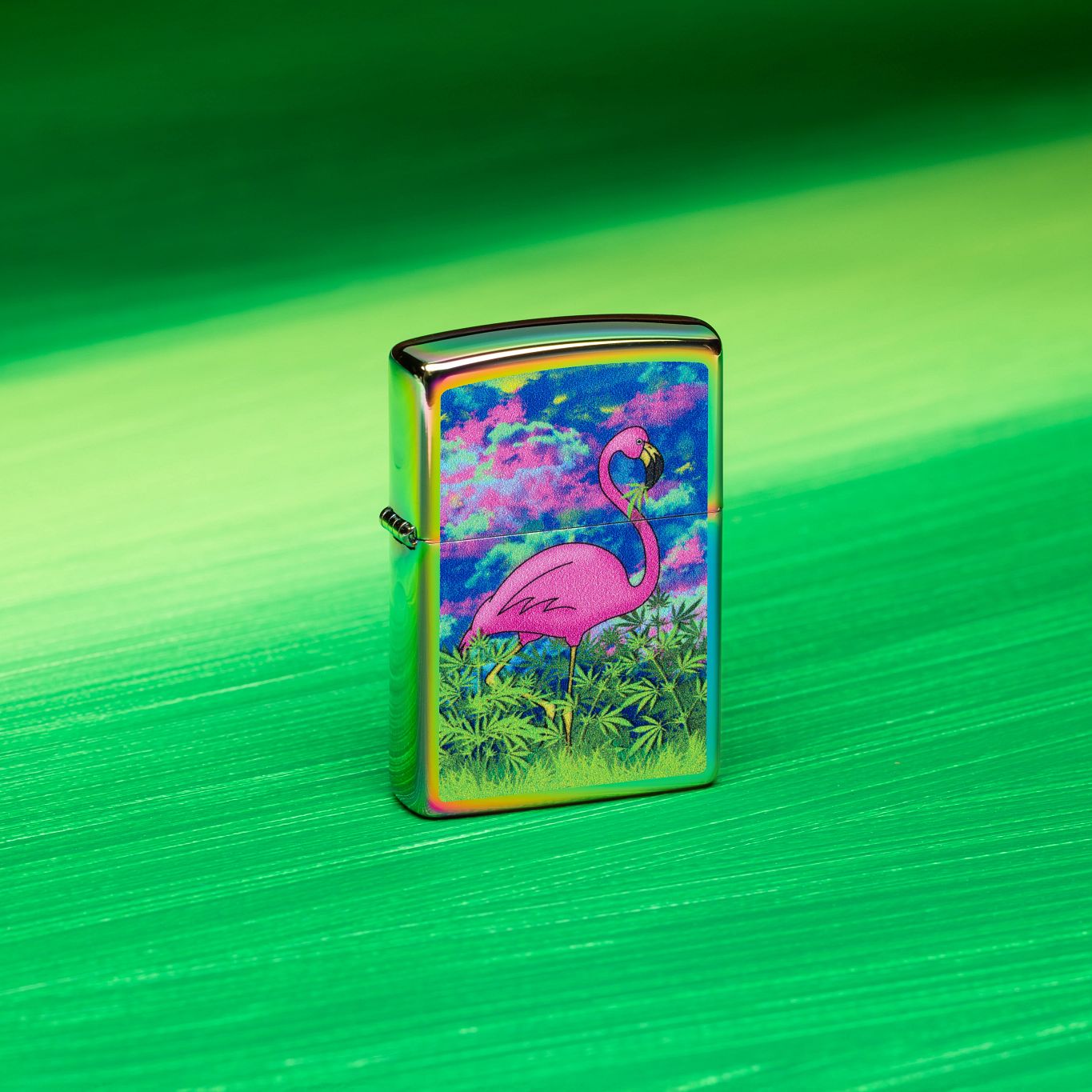 Lifestyle image of Zippo Flamingo Fields Design Multi Color Windproof Lighter standing on a green brushstroke background featuring a range of varying green tones. 


