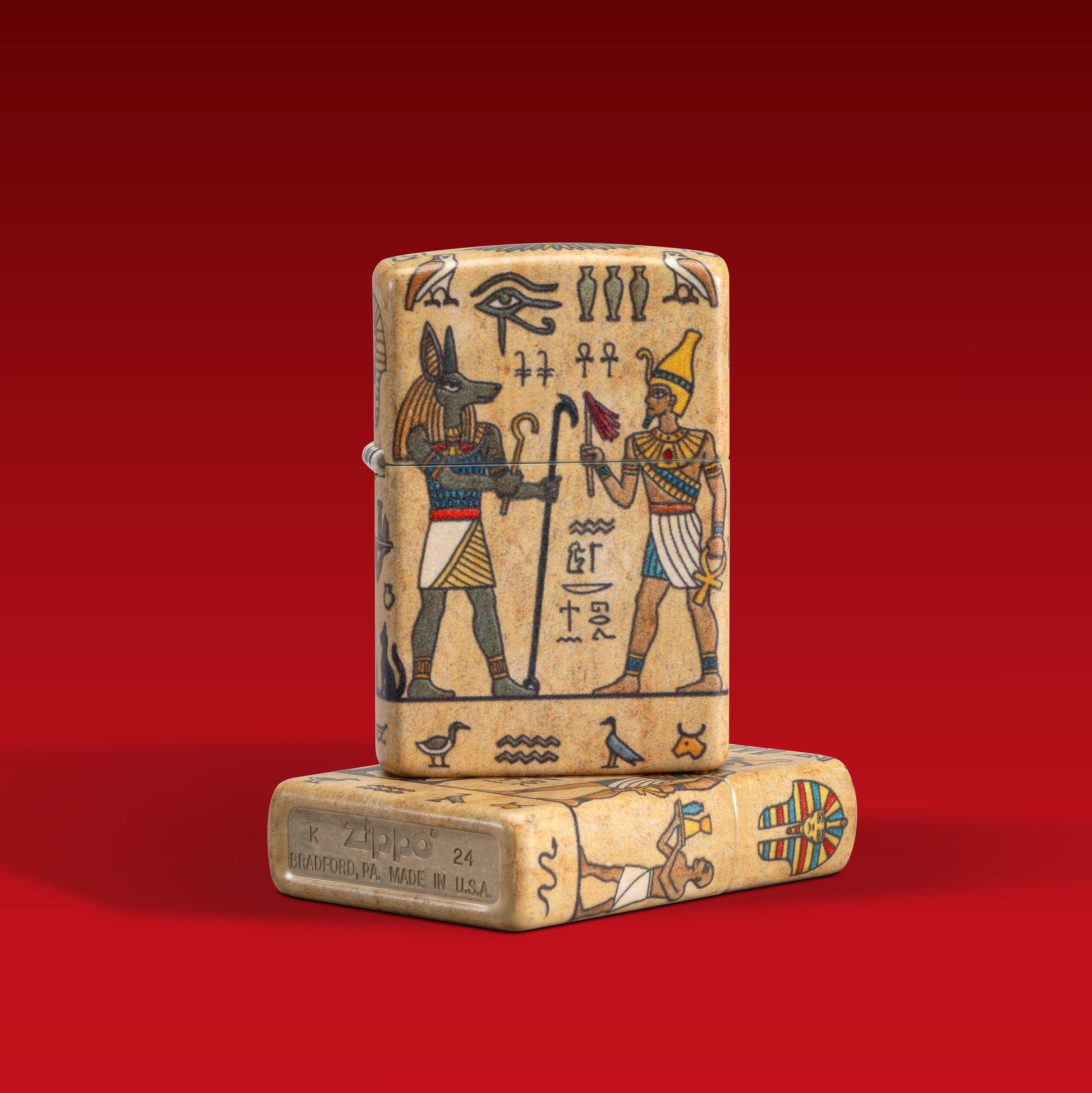 Lifestyle image of two Zippo Ancient Glyphs Design White 540 Matte Windproof Lighters; one lighter lying flat showing the non-hinge and bottom sides of the lighter, while the other lighter is standing on top of the lighter lying flat showing the front of the lighter. 