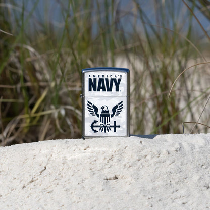 Lifestyle image of Zippo United States Navy® Camo Logo Design Street Chrome Windproof Lighter standing on a grassy sand dune showing the front of the lighter. 

