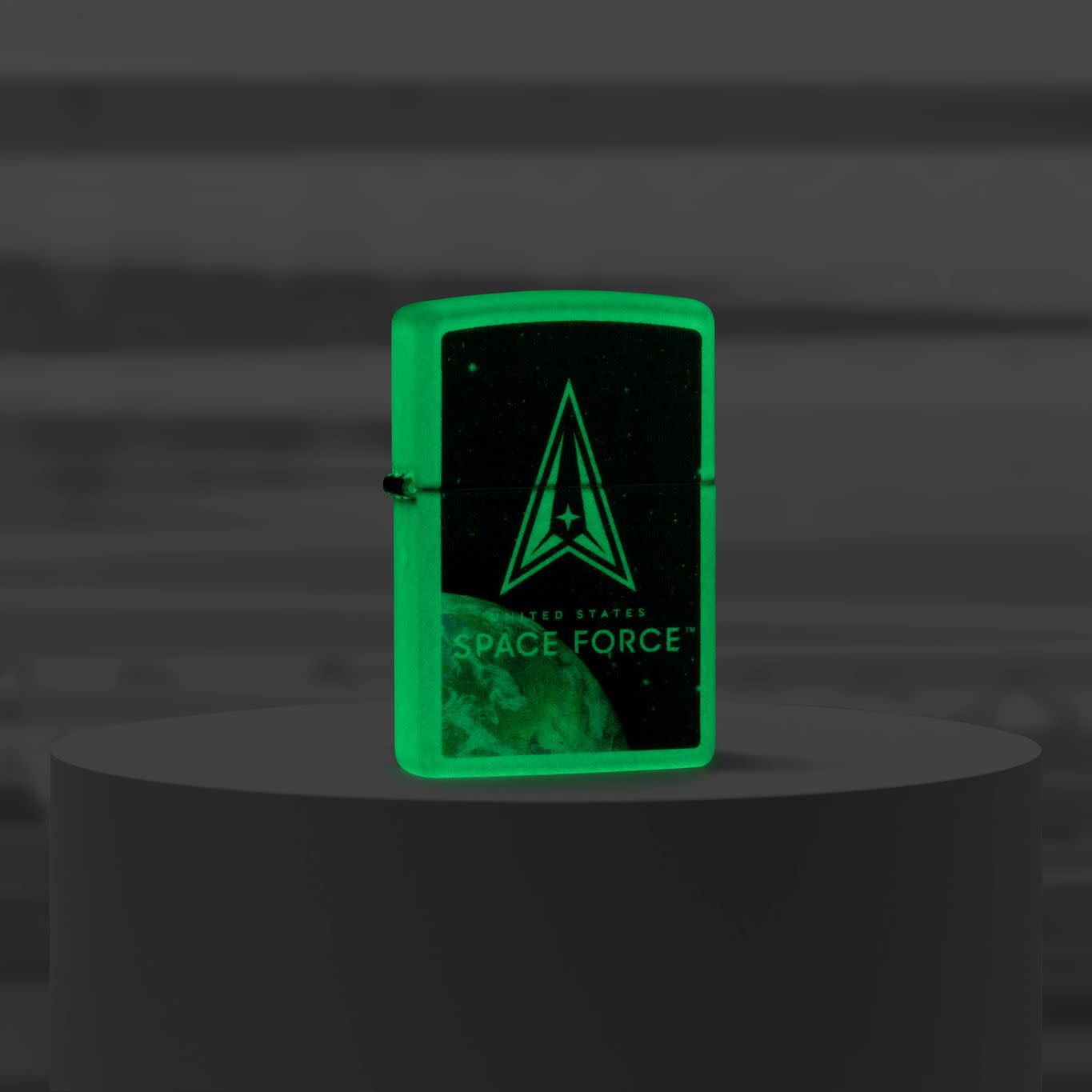 Lifestyle image of Zippo U.S. Space Force™ Glow in the Dark Windproof Lighter standing on a pedestal glowing in the dark.