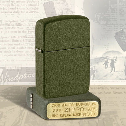 Lifestyle image of two Zippo 2026 Founder’s Day Commemorative Windproof Lighters; one lying flat showing the bottom stamp and hinge side of the lighter while the other lighter is standing on top of the lighter that is lying flat showing the front and hinge side of the lighter with a black and white poster as the background.