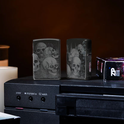 Lifestyle image of two Zippo Skulls High Polish Black Windproof Lighters standing on a VCR player with a candle lit and VHS tape beside them.