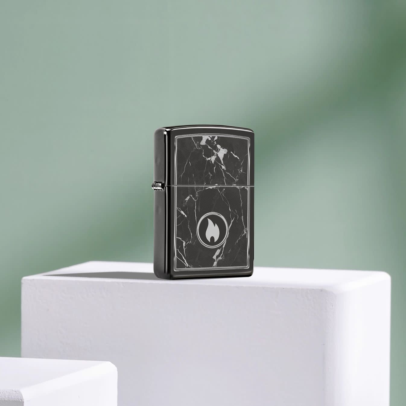 Lifestyle image of Zippo Marble Flame Design High Polish Black Windproof Lighter standing on a white block with a muted green background.