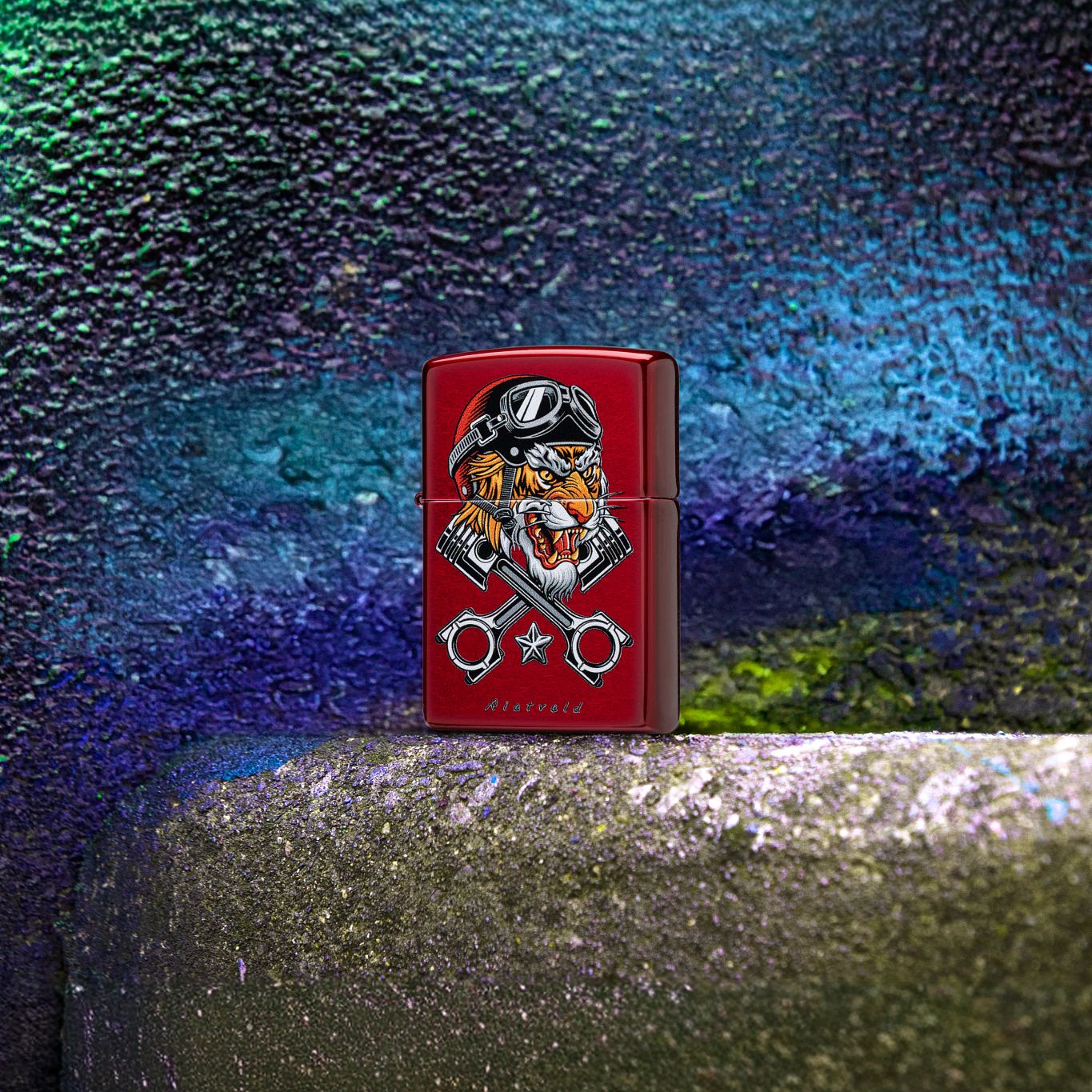 Lifestyle image of Zippo Rietveld Tiger Design Candy Apple Red Windproof Lighter standing on concrete stairs next to graffiti wall art showing the front of the lighter.  

