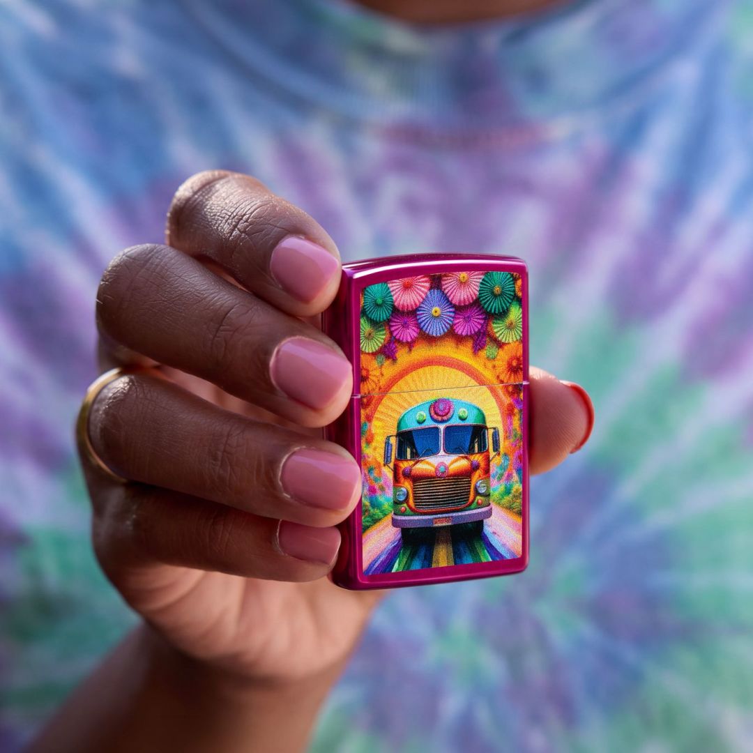 Lifestyle image of Zippo Party Bus Design Candy Raspberry Windproof Lighter being held in hand showing the front of the lighter with a purple, blue and green tie-dye shirt as the background.


