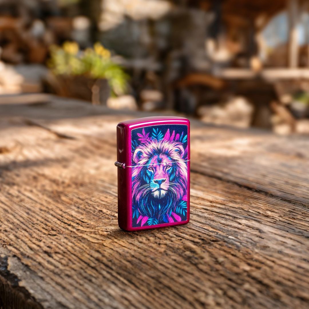 Lifestyle image of Zippo Multicolor Lion Design Candy Raspberry Windproof Lighter standing on a wooden surface showing the front and hinge side of the lighter with an out of focus restaurant as the background.

